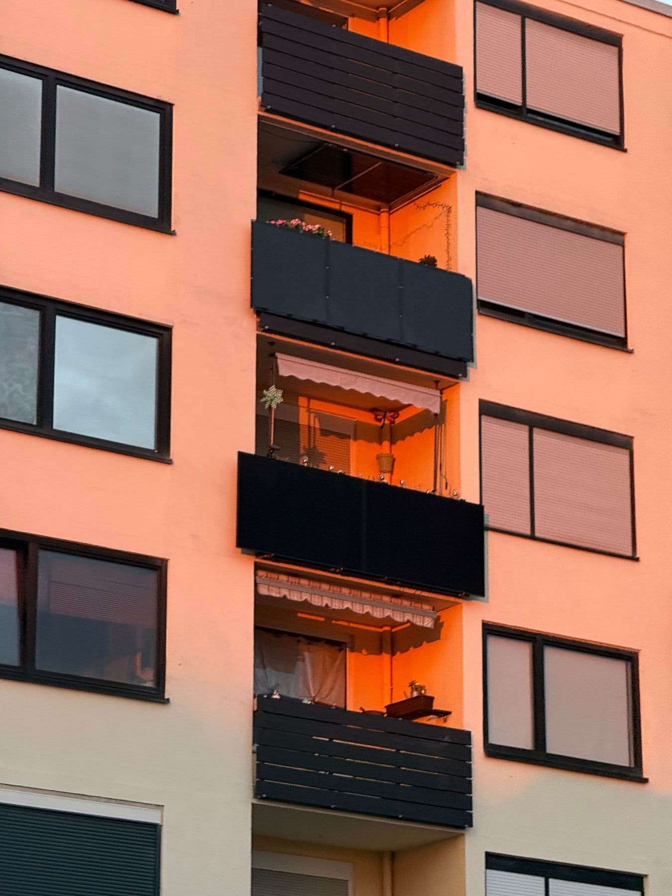 Fachada naranja de un bloque de pisos con persianas enrollables bajadas en varias ventanas y balcones cerrados con paneles oscuros
