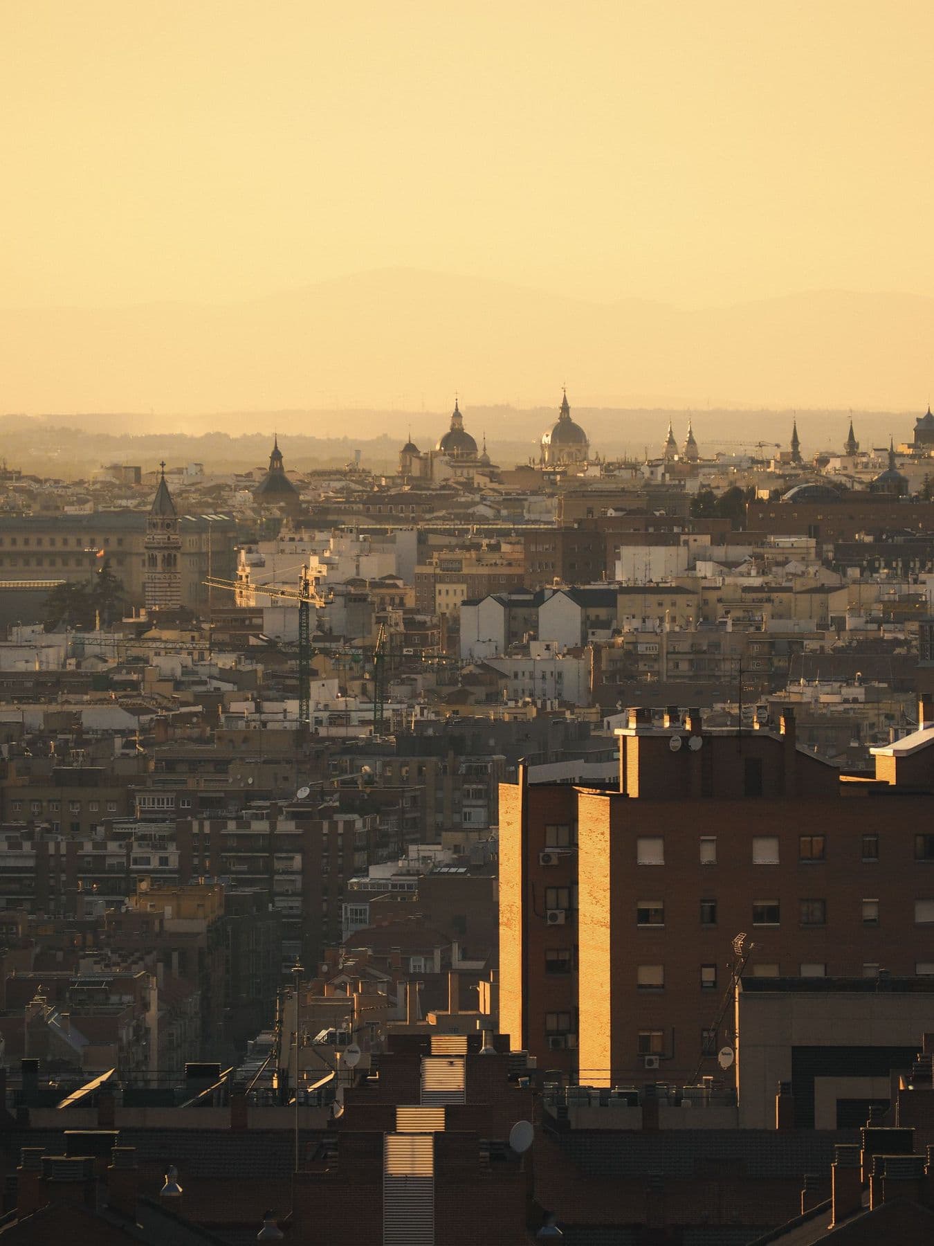 Atardecer dorado sobre una gran ciudad, con cúpulas al fondo entre la bruma y bloques de viviendas iluminados por el sol en primer plano