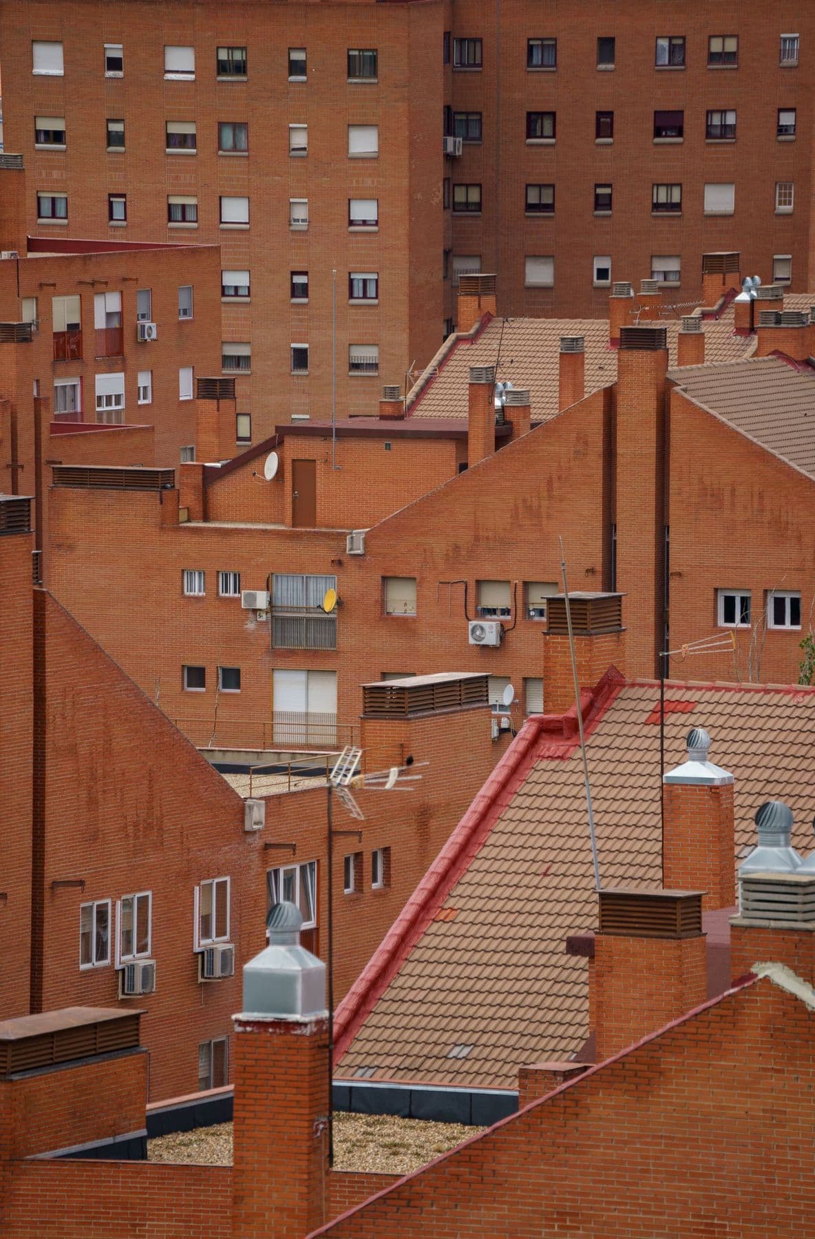 Tejados y fachadas de ladrillo de varios bloques de viviendas, con chimeneas, antenas y ventanas con persianas vistas desde lo alto