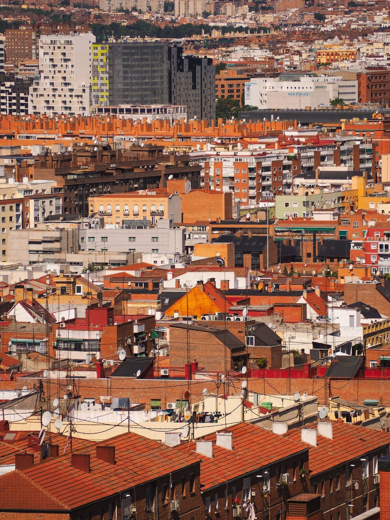 Vista desde lo alto de una ciudad densa con tejados de teja, azoteas, antenas y bloques de viviendas de ladrillo hasta el horizonte