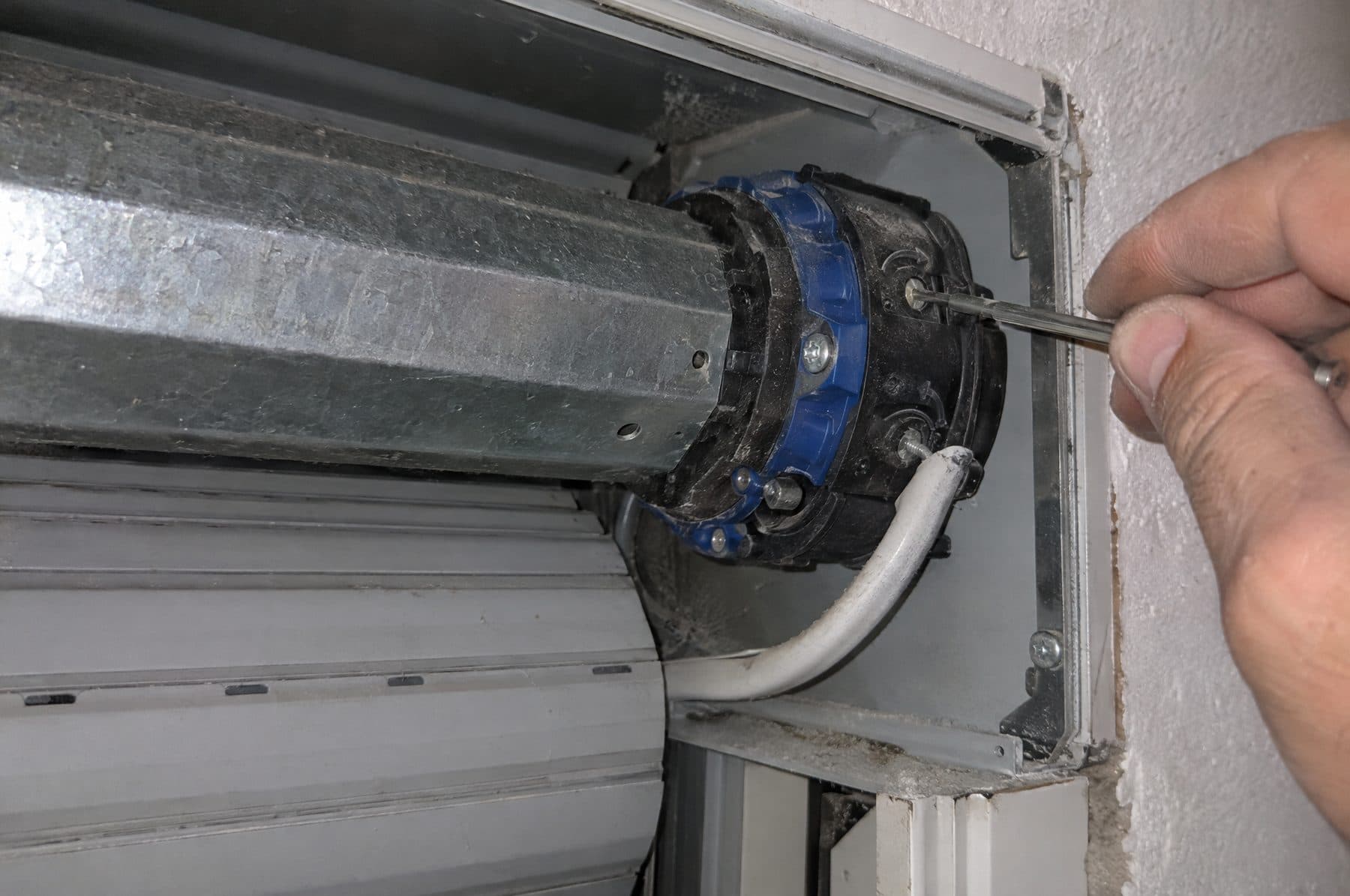 Destornillador fino ajustando los tornillos de final de carrera en la cabeza de un motor tubular dentro del cajón de una persiana