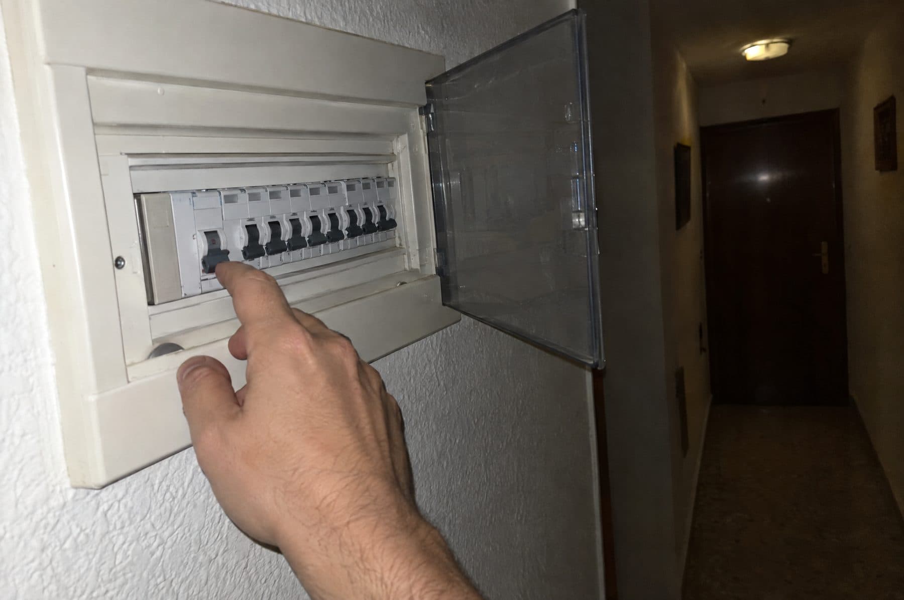 Mano junto al cuadro eléctrico de un pasillo, con la tapa abierta y uno de los interruptores bajado