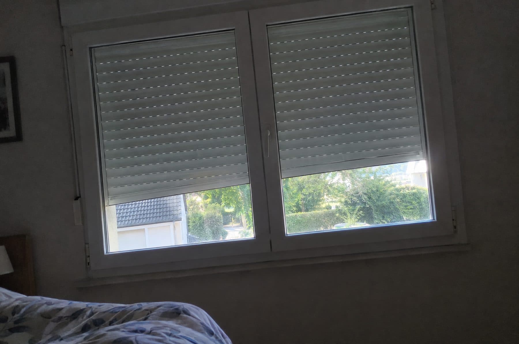 Ventana de dormitorio con dos persianas de PVC detenidas a media altura, vistas desde dentro