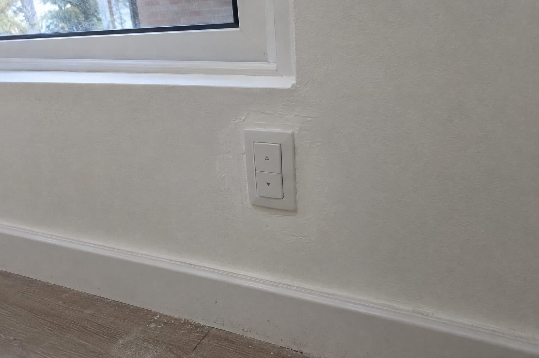 Pulsador de subir y bajar persiana recién colocado en la pared bajo la ventana, con la masilla blanca del parcheo aún sin pintar